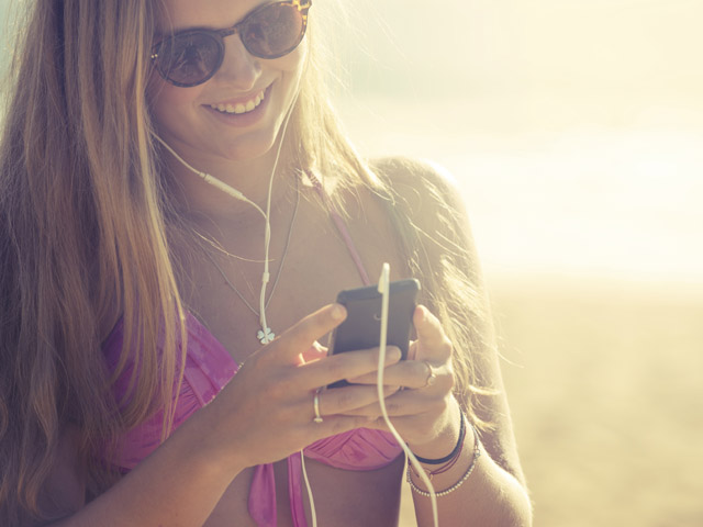 Young woman with phone and earphones at the beach